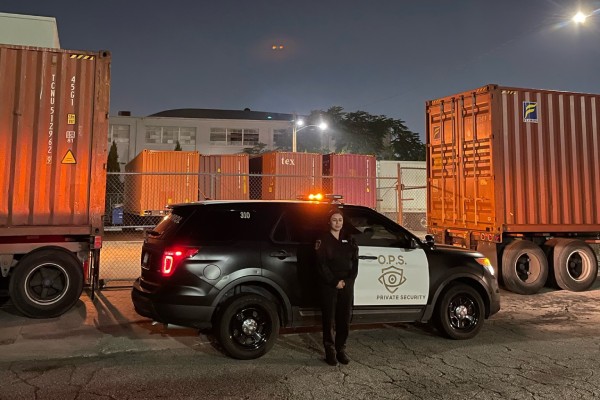 OPS Logistical Security staff guard standing next to patrol vehicle